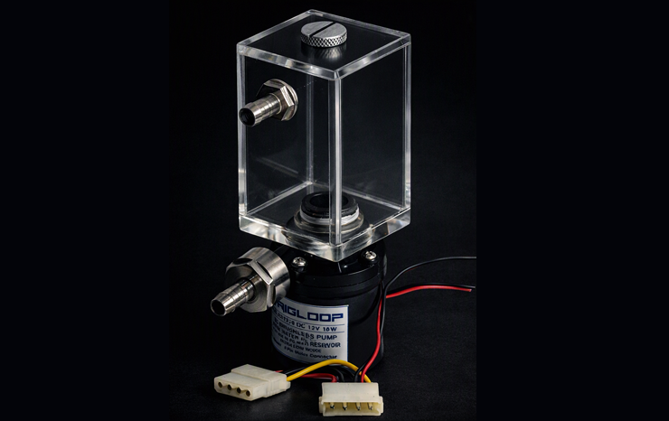 A computer liquid cooling pump and reservoir assembly illuminated by cool bluish‑white light against a dark background. The transparent acrylic reservoir with metal fittings sits atop a black cylindrical pump labeled “RIGLOOP DC 12V 18W.” Power cables and connectors extend from the pump, resting on a dark surface